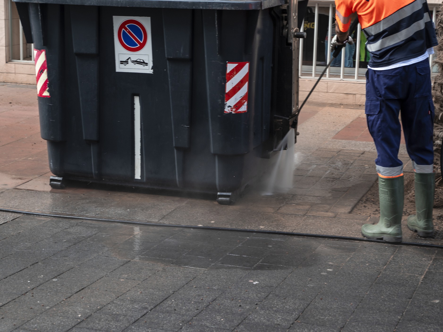 Sanitation worker spraying sidewalk near dumpster