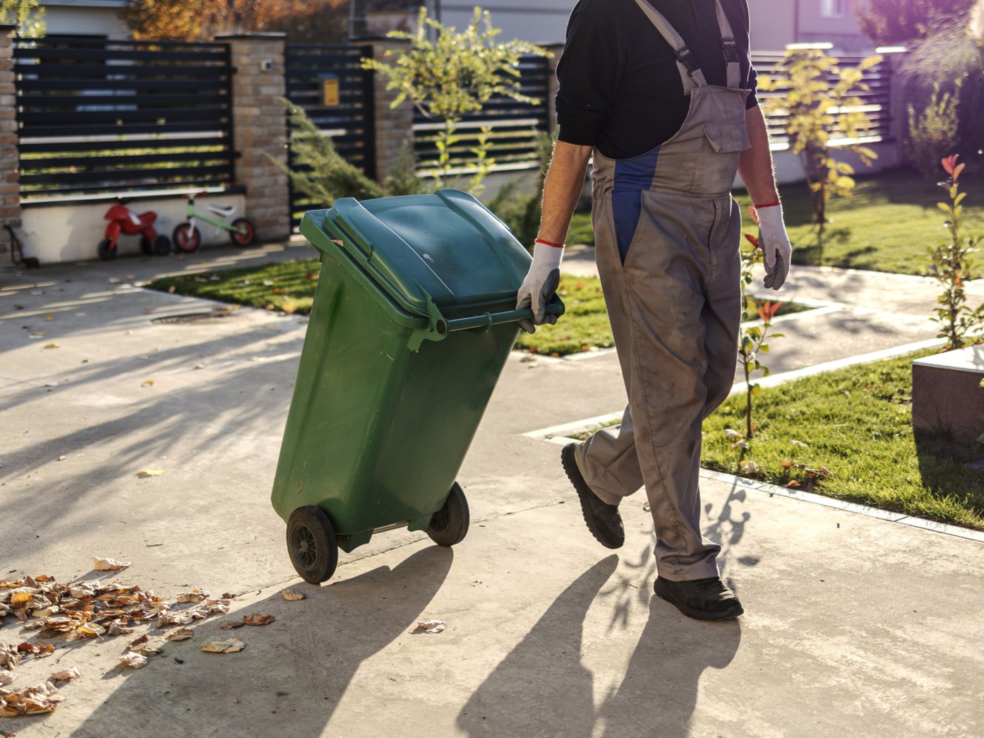 Worker handling waste container in driveway