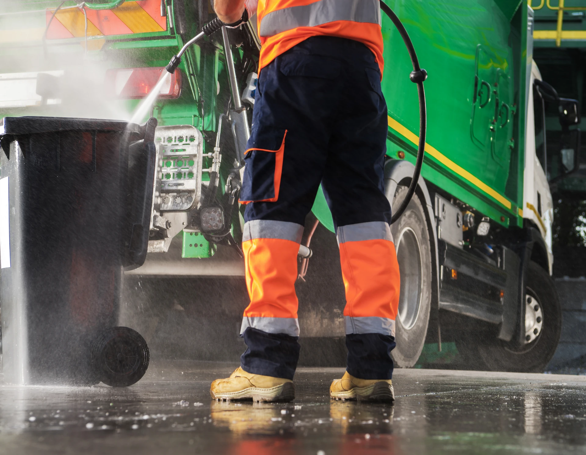Worker cleaning garbage bin with pressure washer